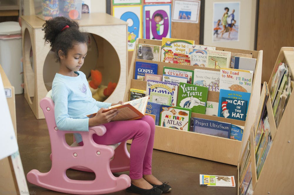 Child sitting in a pink rocking chair reading a book in a classroom