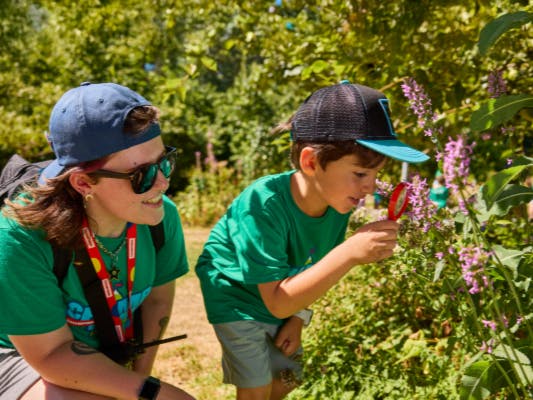 Child looking at flowers through a magnifying glass next to an adult