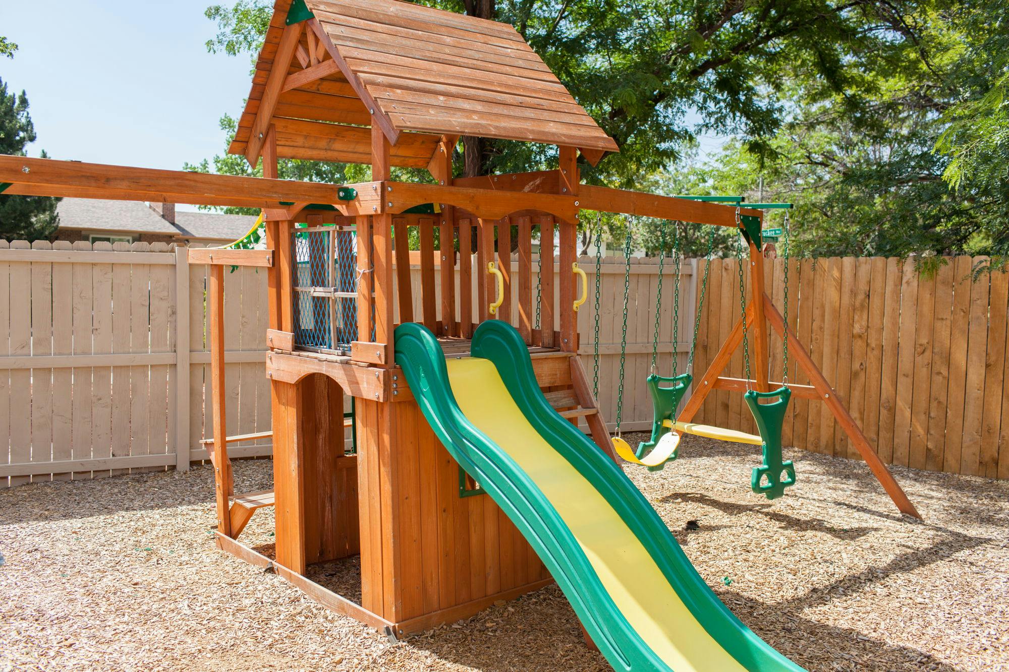 Wooden playground with a green and yellow slide and swings