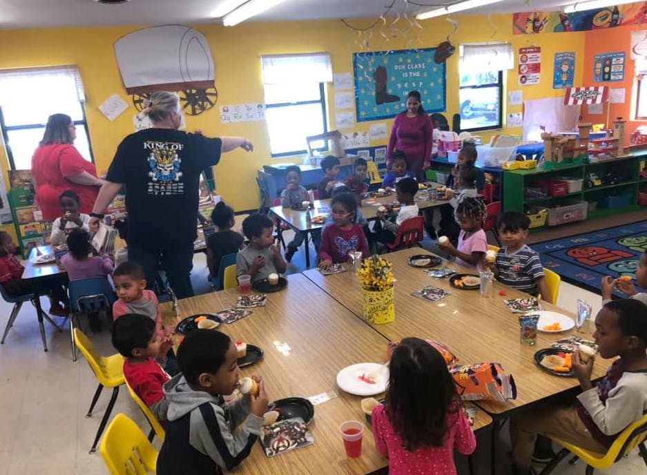Adults supervising children eating at tables in a classroom