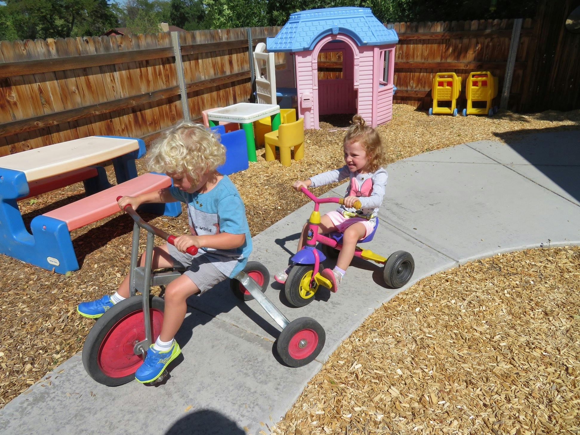 Two children riding tricycles on a paved path