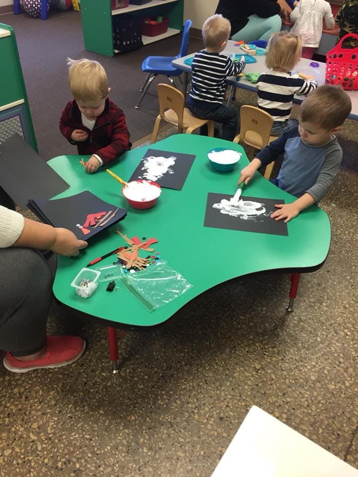 Children doing crafts at a green table in a classroom