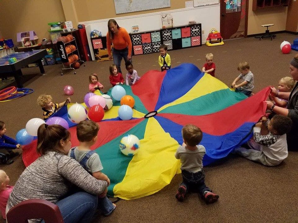 Adults and children playing with a colorful parachute and balloons indoors