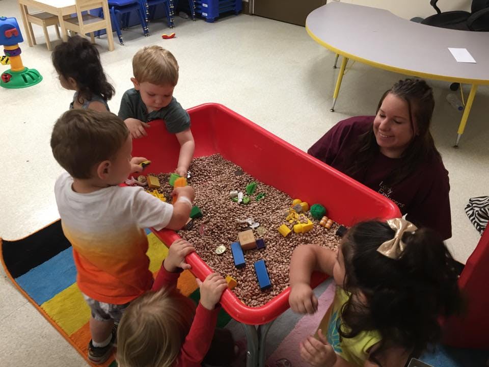 Adult and children playing with sensory bin in a classroom