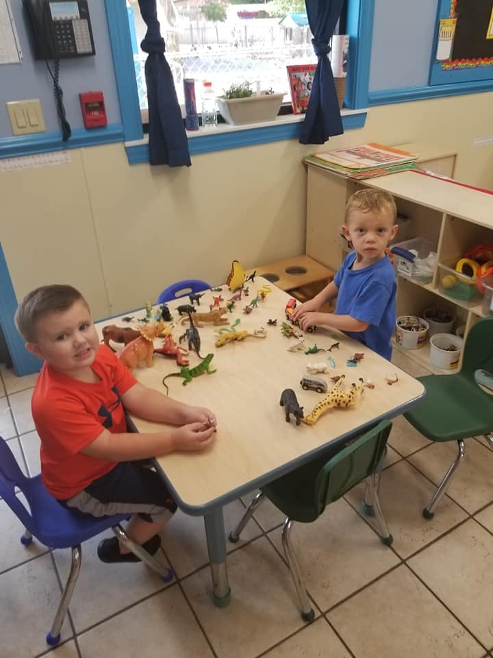 Two children playing with animal toys at a table in a classroom