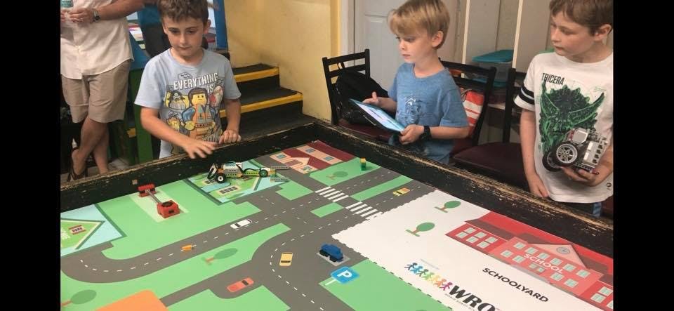 Three children playing with toy cars on a mat with a road map