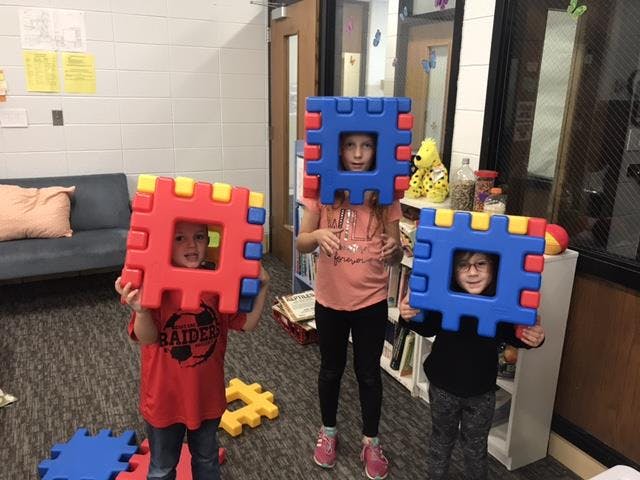 Three children holding large interlocking block pieces in front of their faces