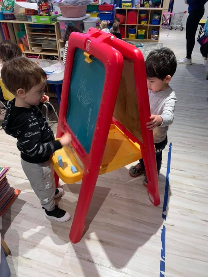 Two children playing with a red easel in a classroom