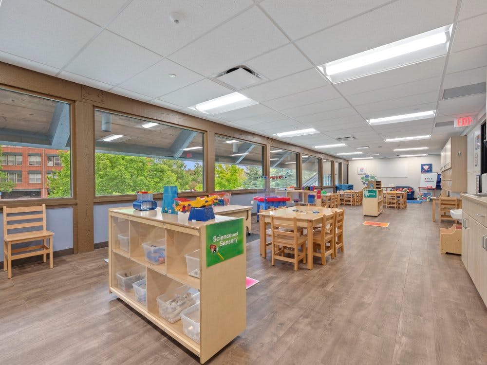 Classroom with small wooden tables and chairs, and a \"Science and Sensory\" shelf