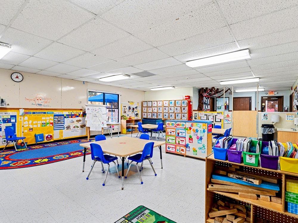 An empty classroom with small tables and chairs, bright blue carpet