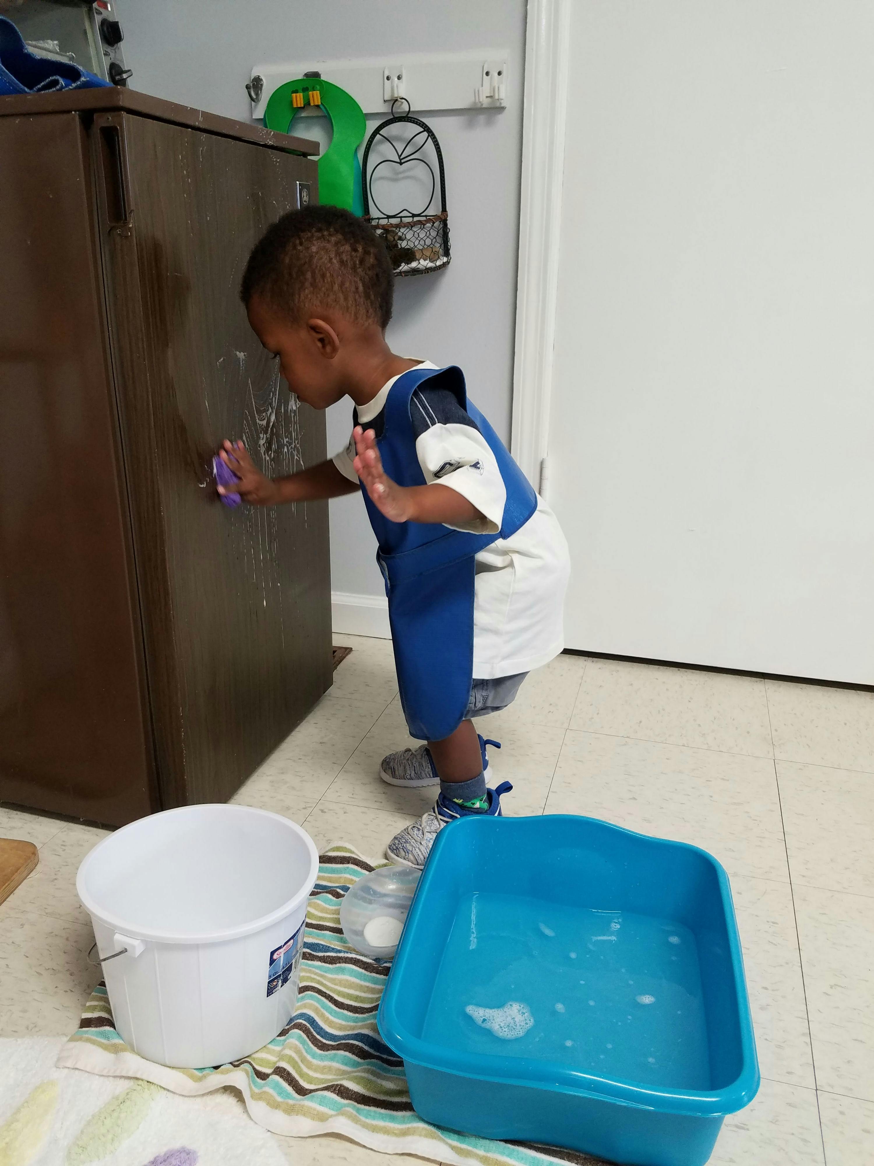 Child cleaning a cabinet with a sponge