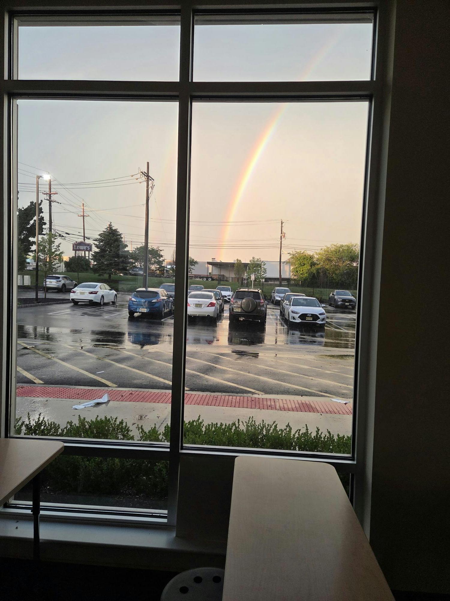 A rainbow over a parking lot seen from a window