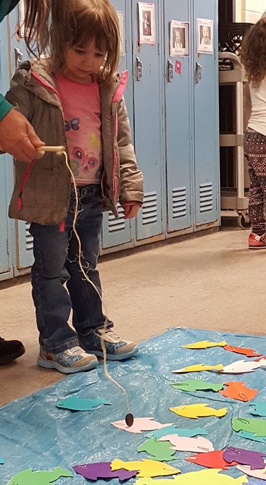 Child playing a fishing game with paper fish on a blue tarp