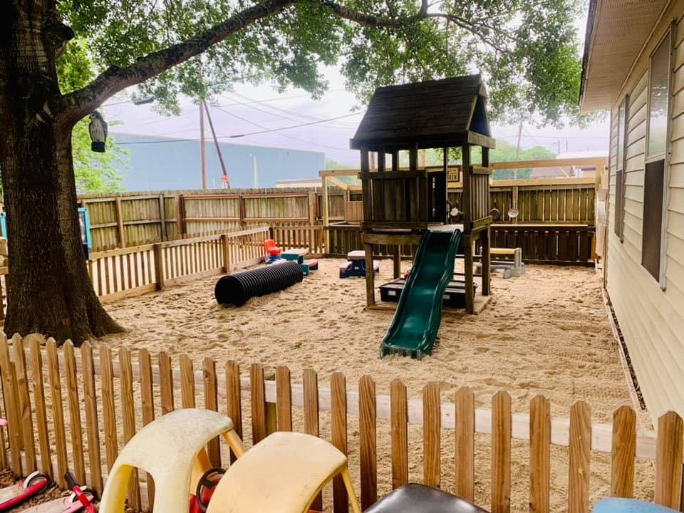 Outdoor playground with sand, wooden play structure with slide, and fence