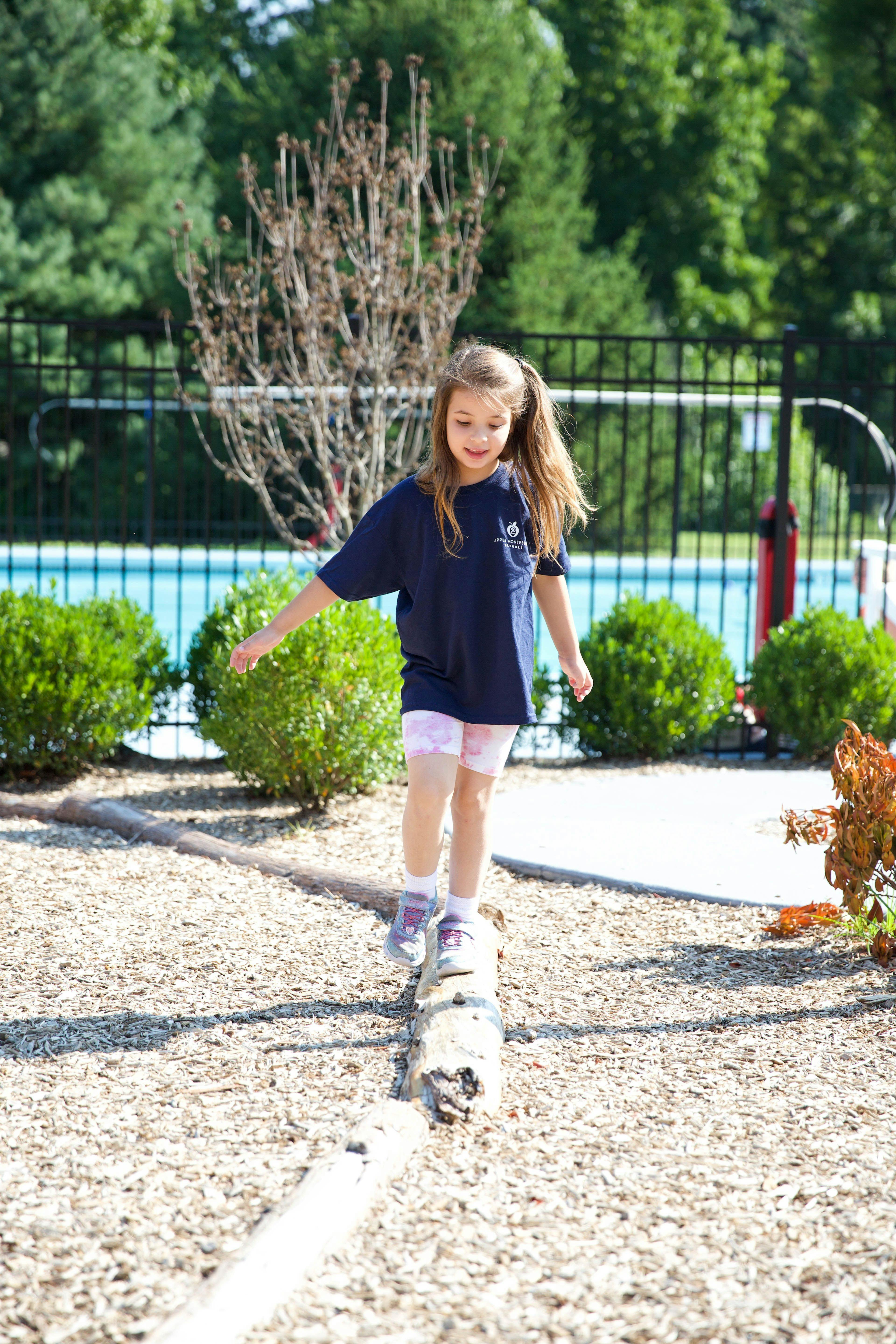 Child walking on a wooden balance beam over wood chips