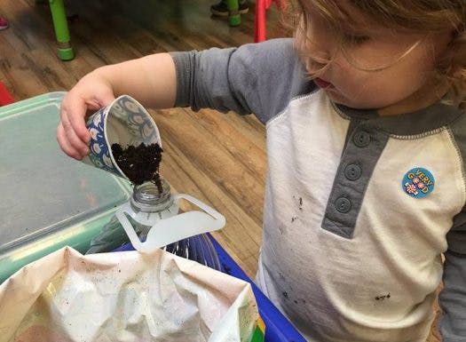 Child pouring soil from a cup into a funnel