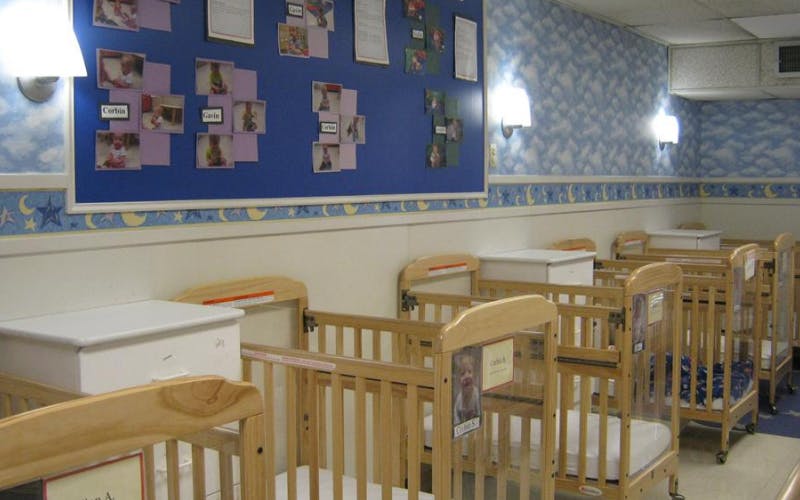Room with multiple wooden cribs and a bulletin board with child photos