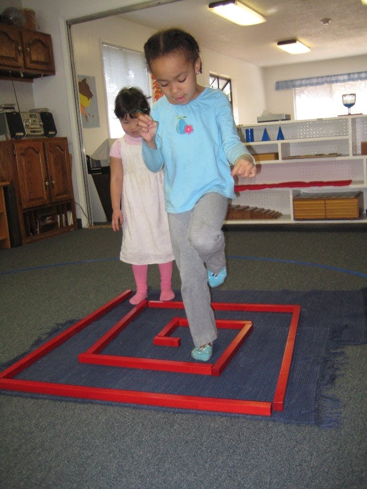 Child stepping over red blocks on a blue mat, another child standing nearby
