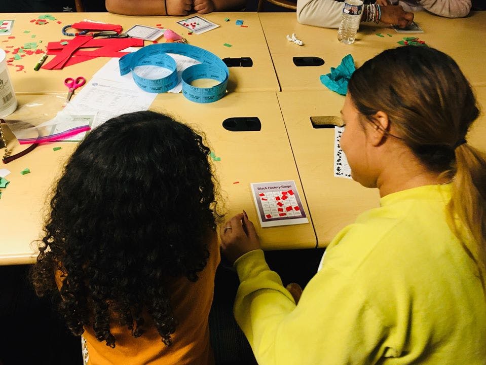 Two people at a table with craft supplies, looking at a card