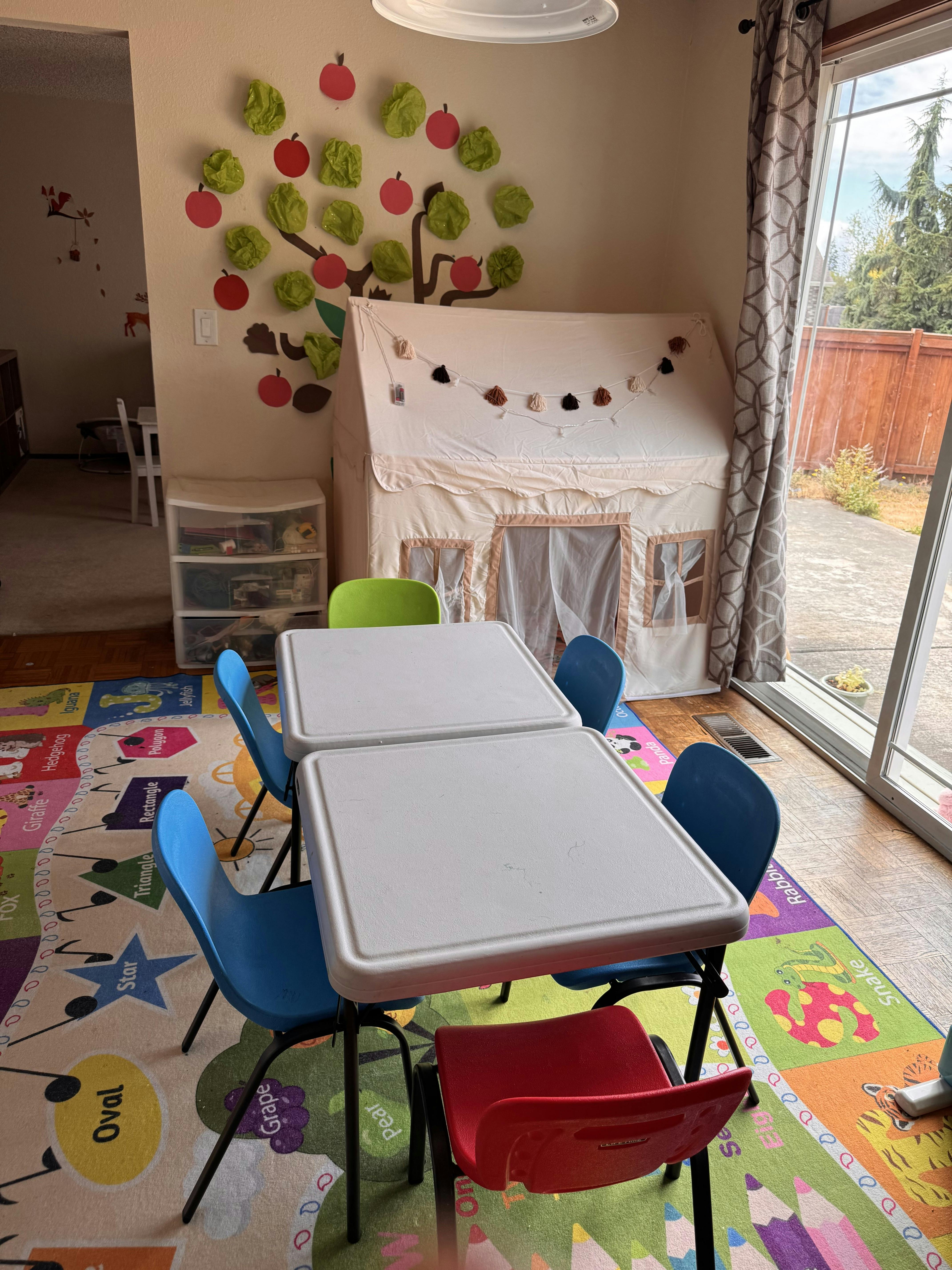 Children's play area with small tables and chairs, a play tent, and a colorful rug