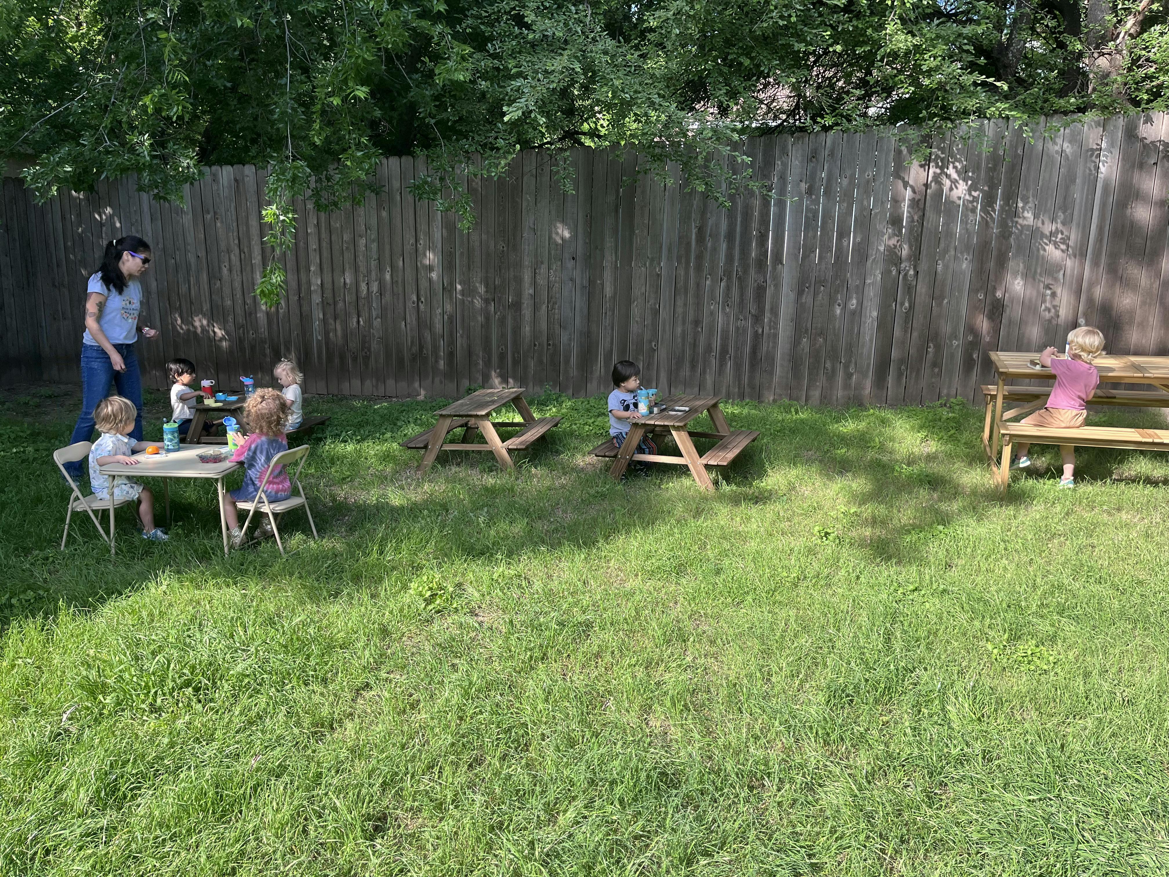 Adult and children at small picnic tables in a grassy area