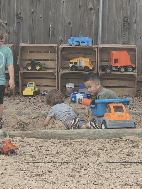 Two children playing in a sandbox with toy trucks