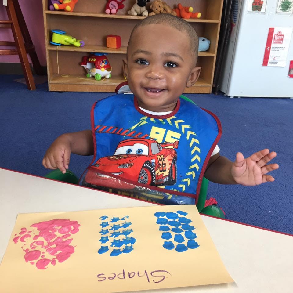 Child in a bib sitting at a table with a paper showing shapes