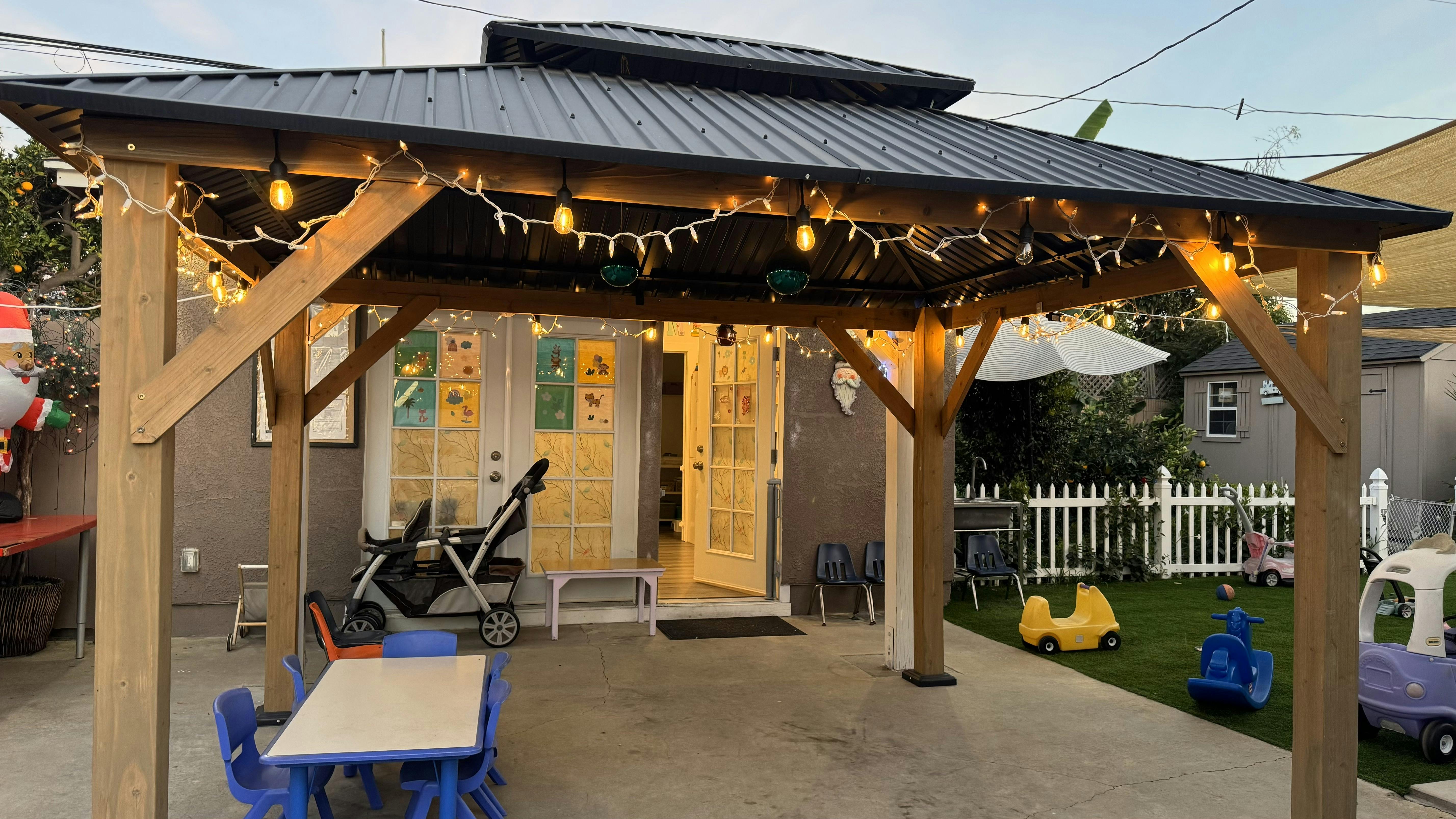 Outdoor patio with a wooden gazebo and string lights, children's toys on artificial grass