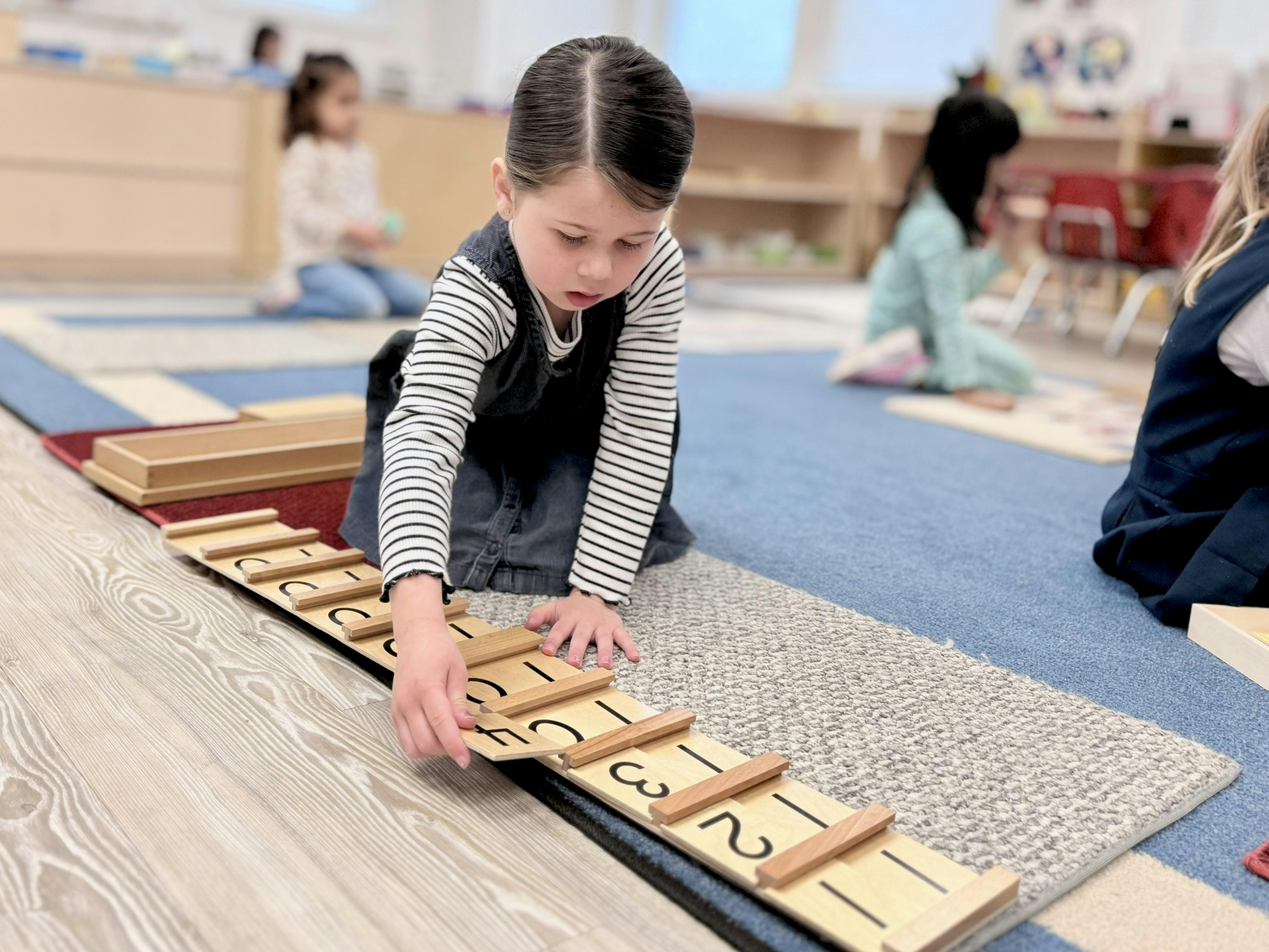 Child on a classroom floor working with wooden number blocks