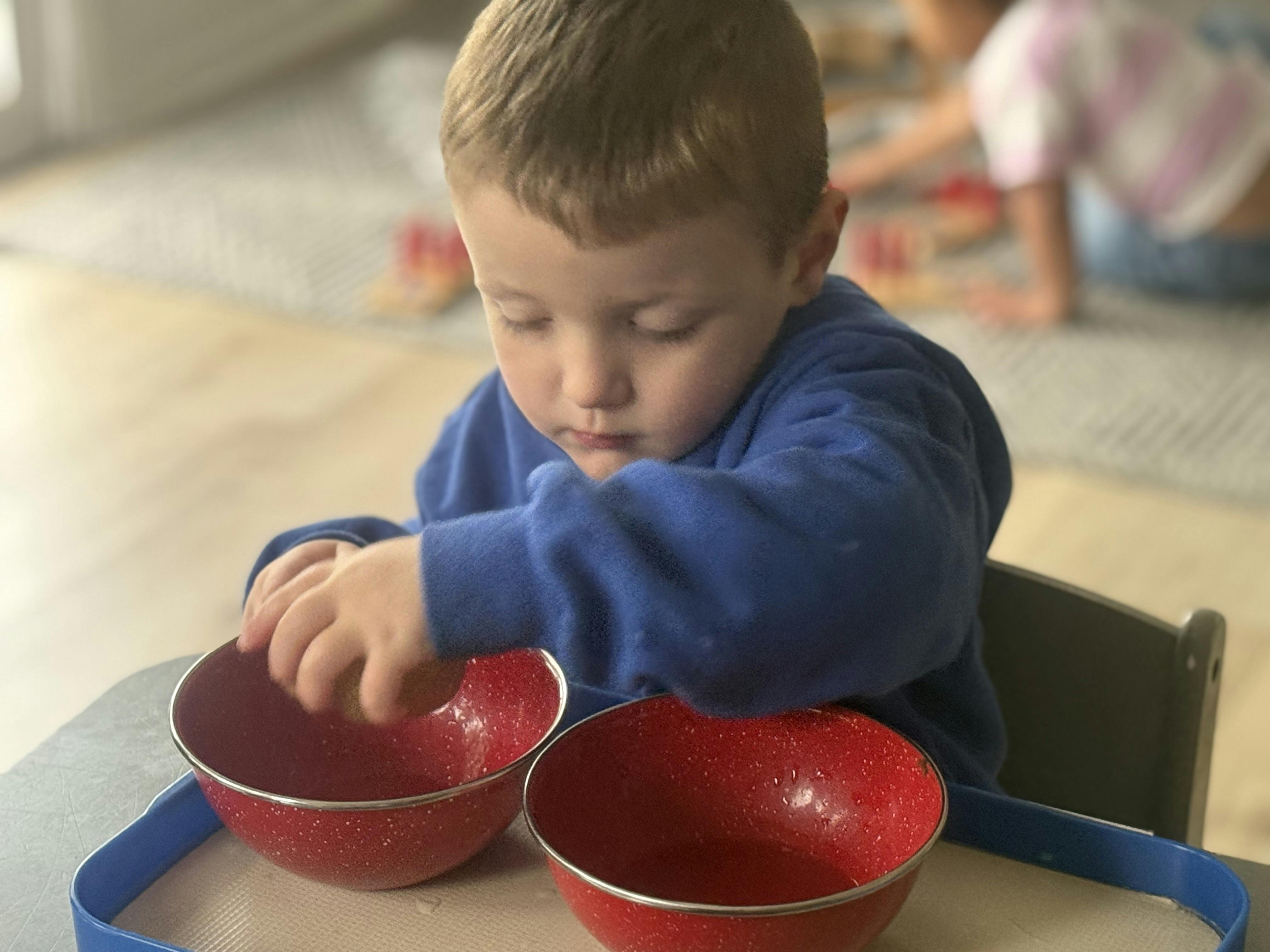 Child sitting at a table transferring objects between two red bowls