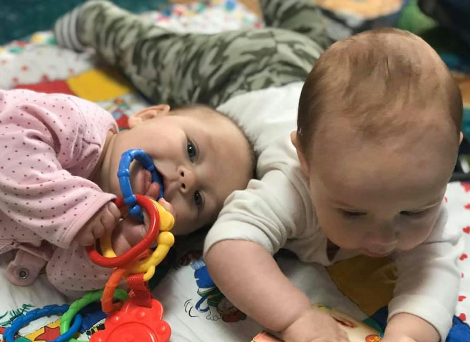 Two babies playing with toys on a blanket