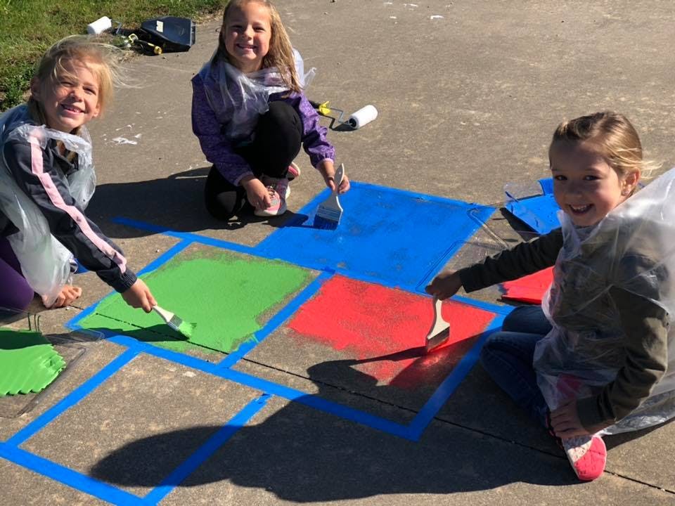 Three children painting colorful squares on pavement