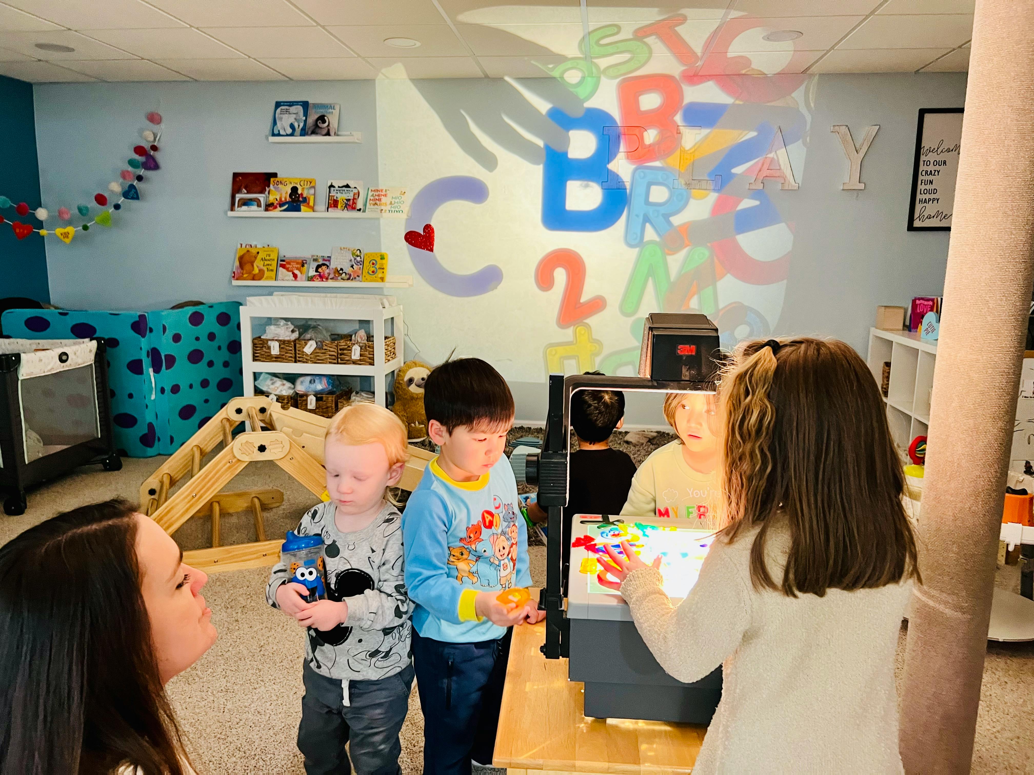 Three children and an adult in a room with projected letters on the wall
