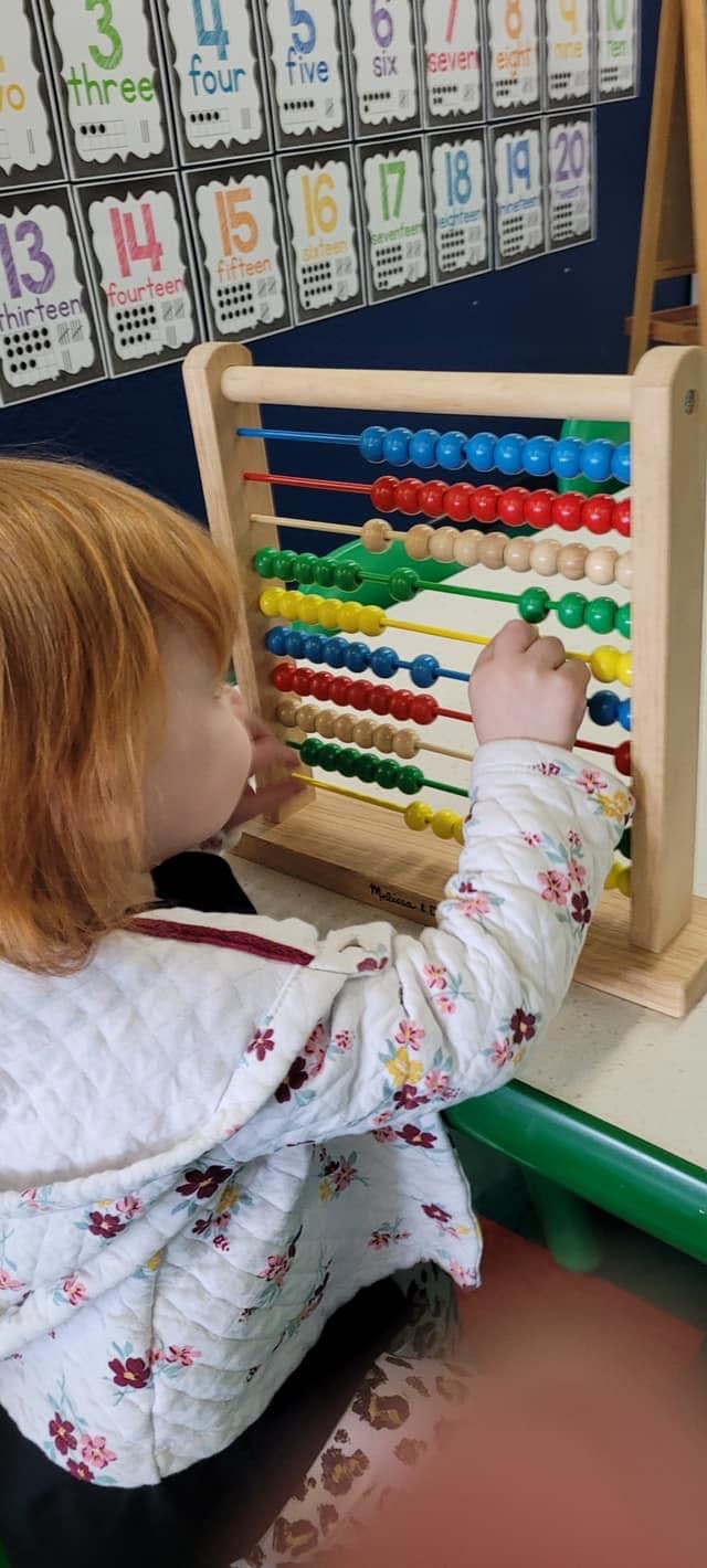 Child playing with a colorful abacus in a classroom
