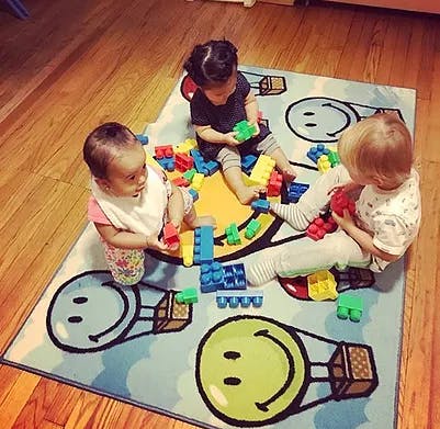 Three children playing with colorful building blocks on a rug