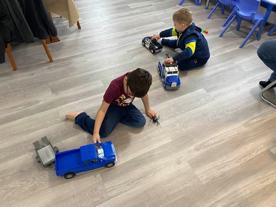 Two children playing with toy trucks on a wooden floor
