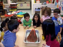 Children gathered around a table watching a volcano science experiment