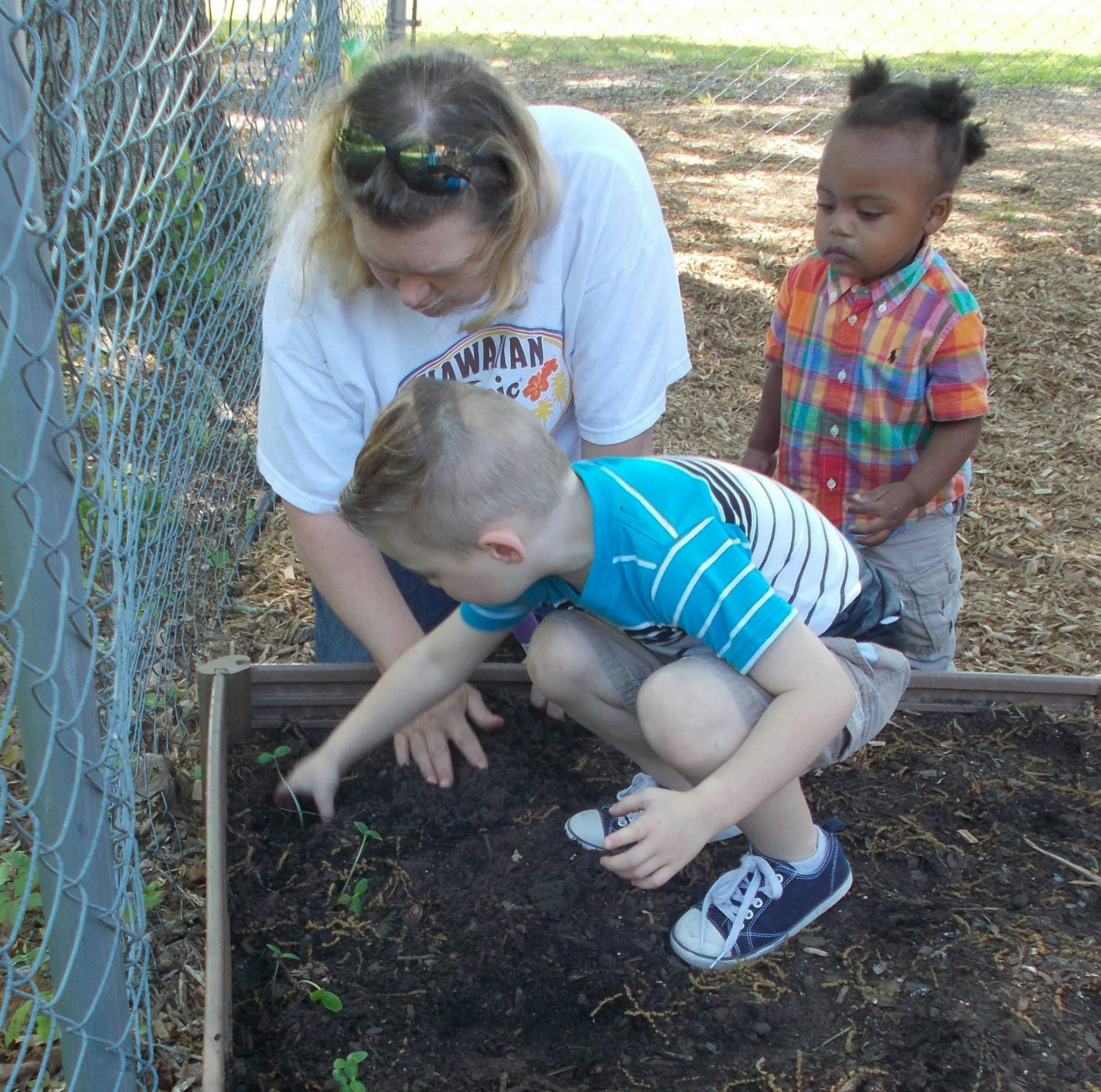 Person and two children planting in a garden bed