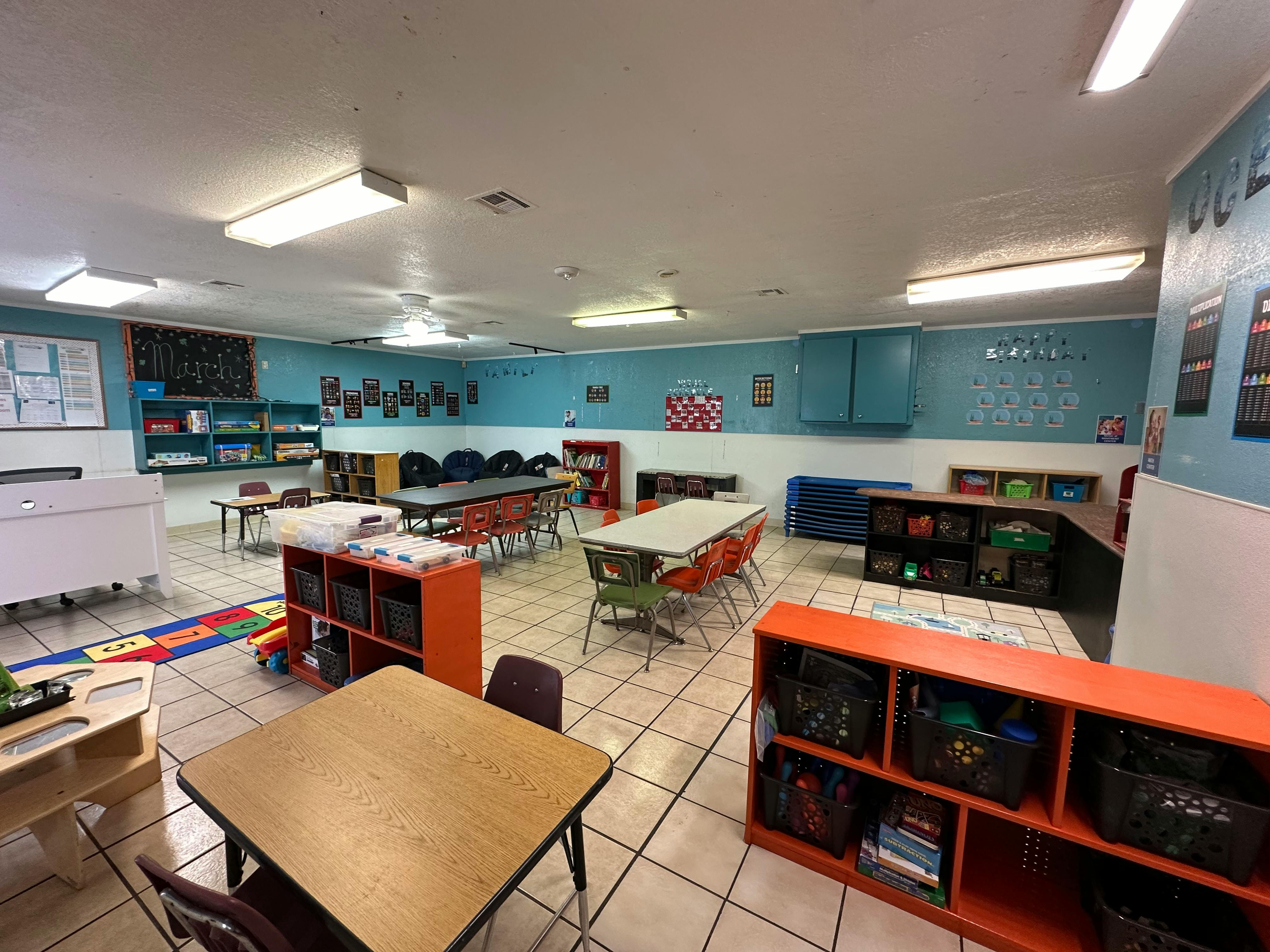 Classroom with multiple tables and chairs, and storage shelves