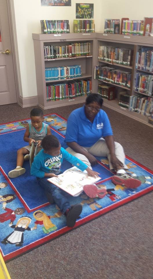 Adult and two children sitting on a rug reading books in a library