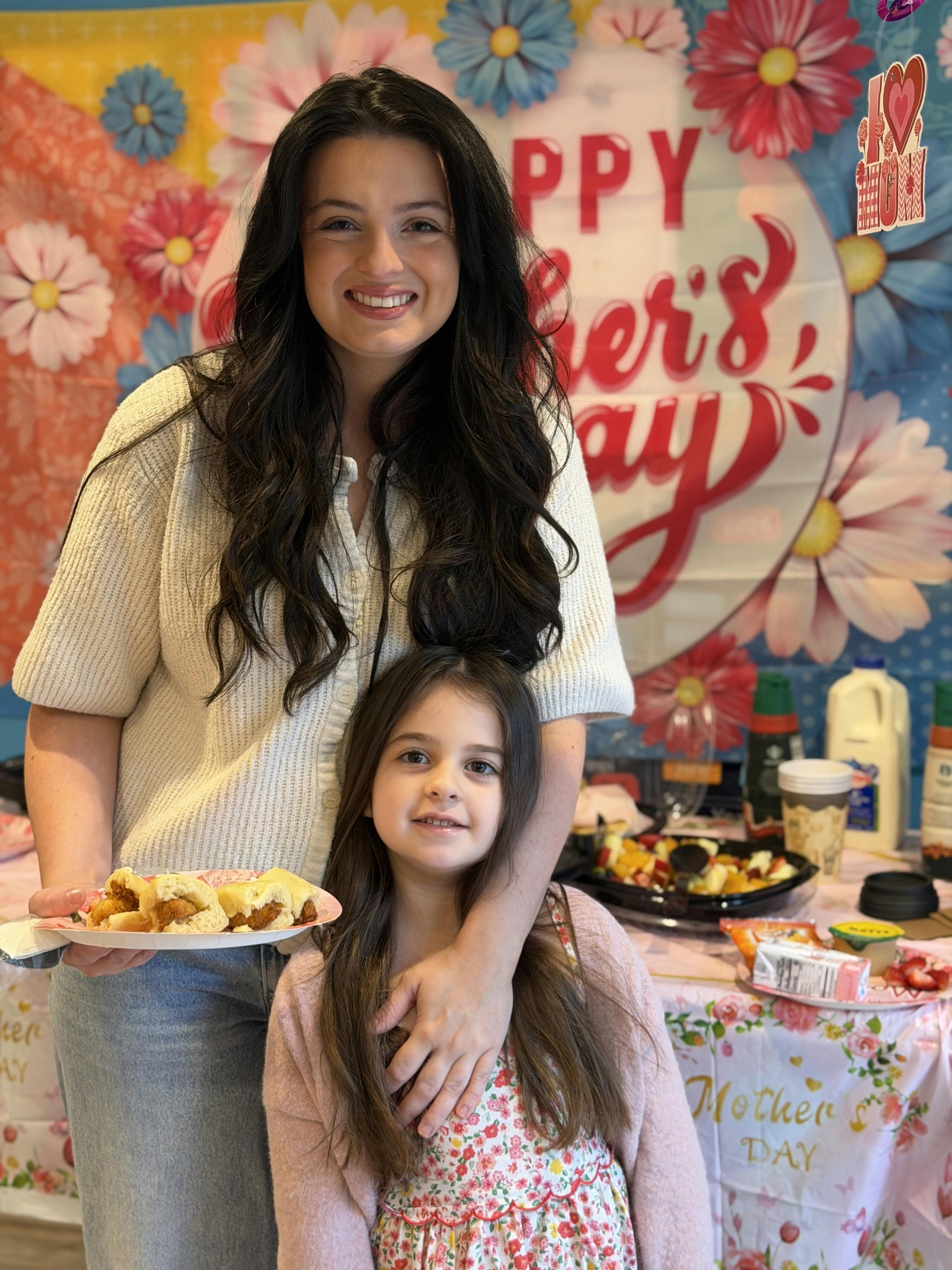 Smiling person holding a plate of chicken sliders with a child next to them