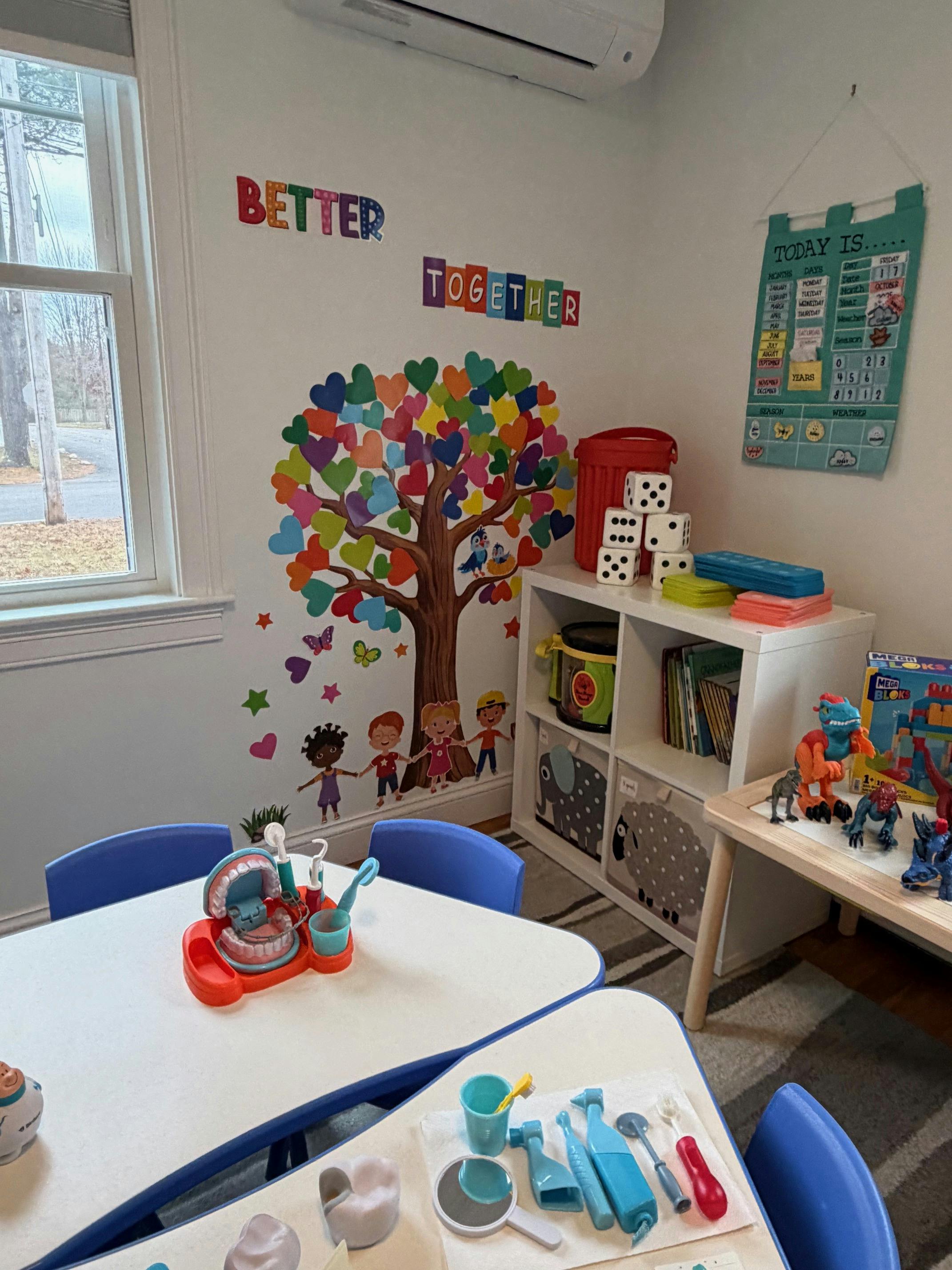 Classroom with a colorful tree mural, tables, and toys