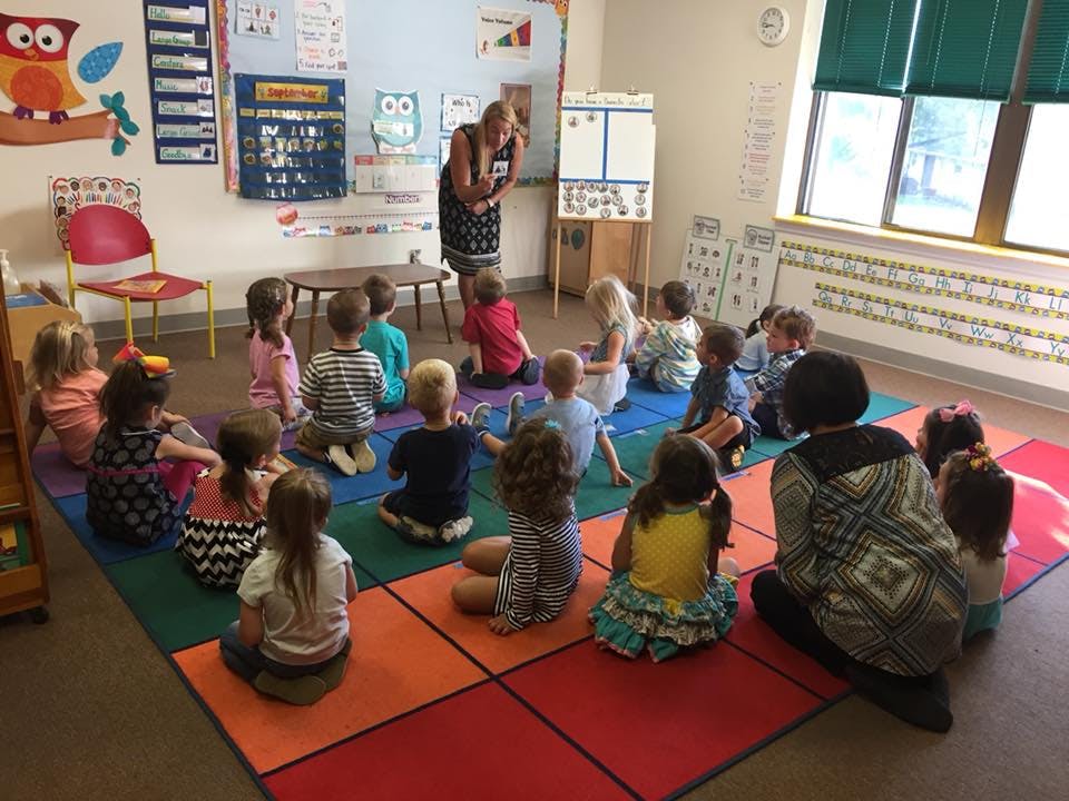 Adults and children sitting on a colorful mat in a classroom