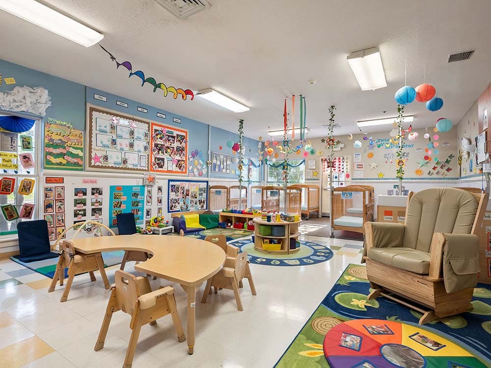 Classroom with child-sized tables, cribs, a rocking chair, and colorful decorations