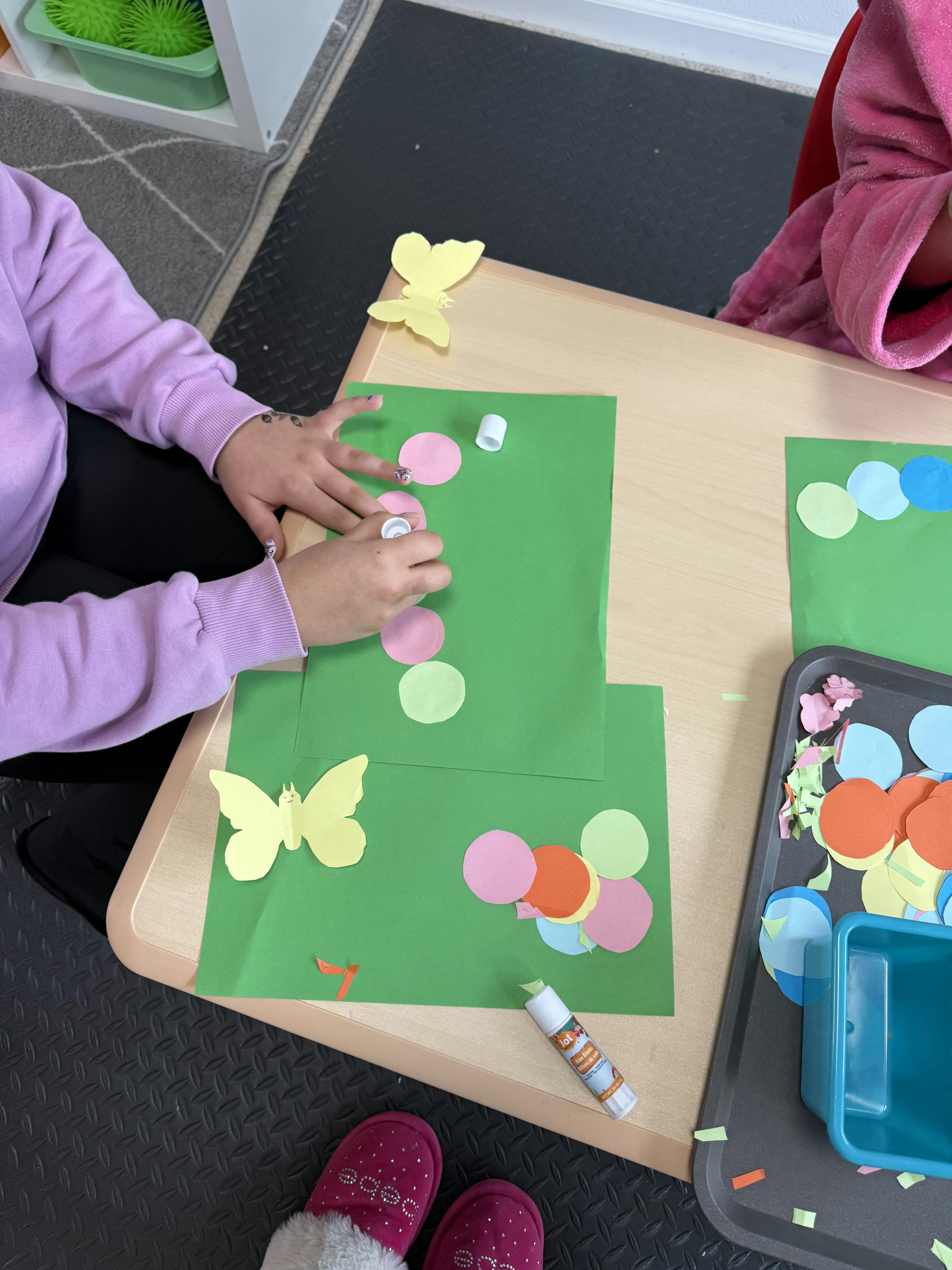 Person gluing paper cutouts onto green paper