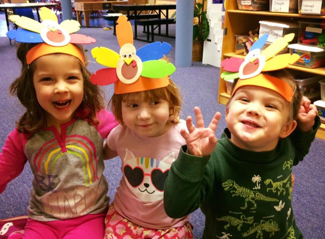 Three children wearing colorful turkey headbands in a classroom