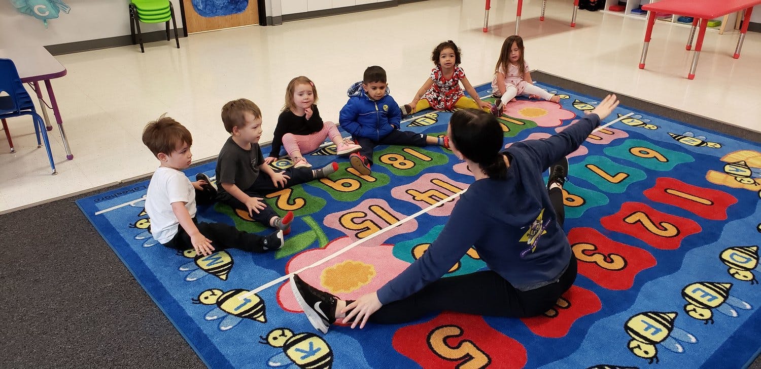 Adult and children sitting on a rug, adult stretching