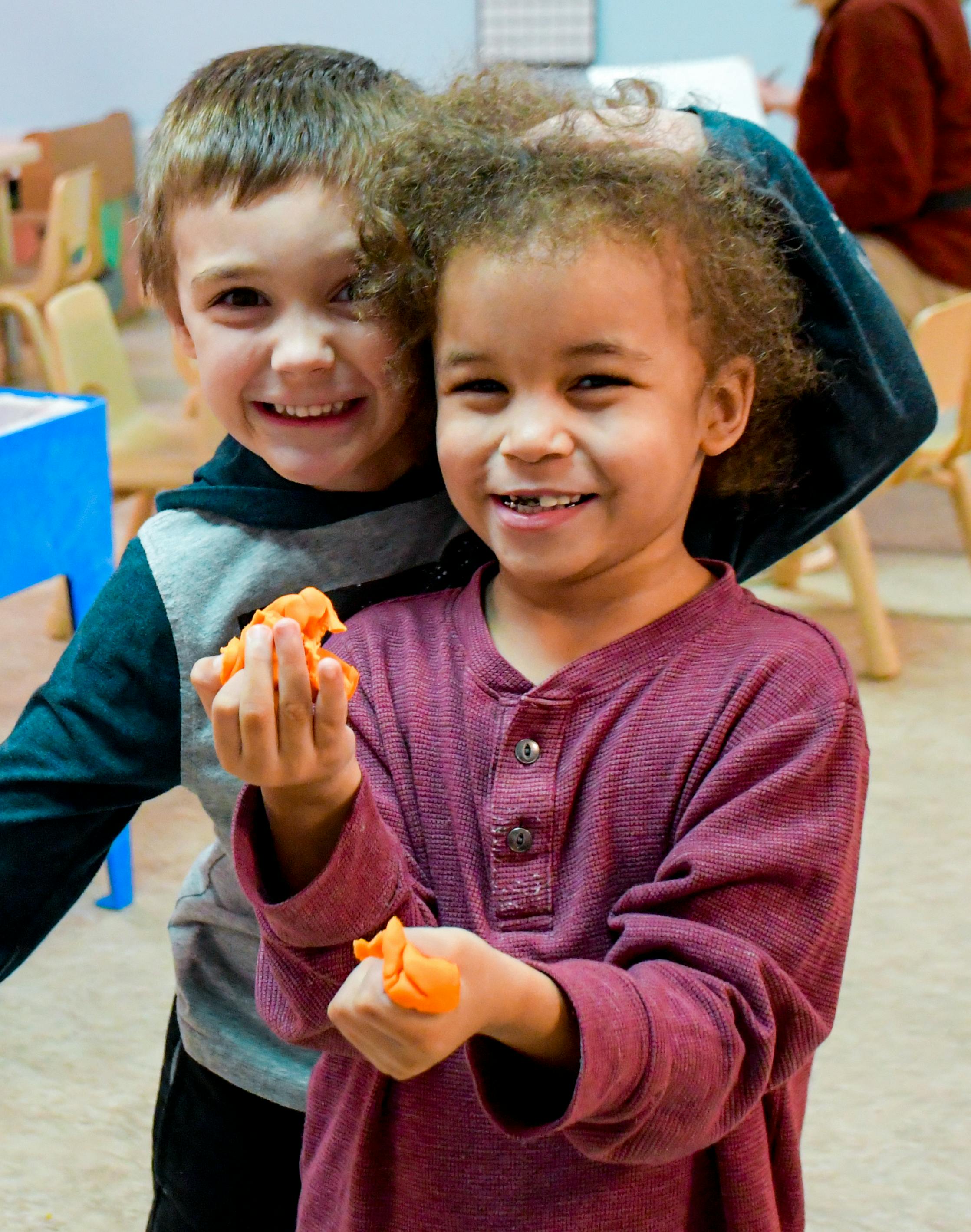 Two children smiling, one holding orange objects