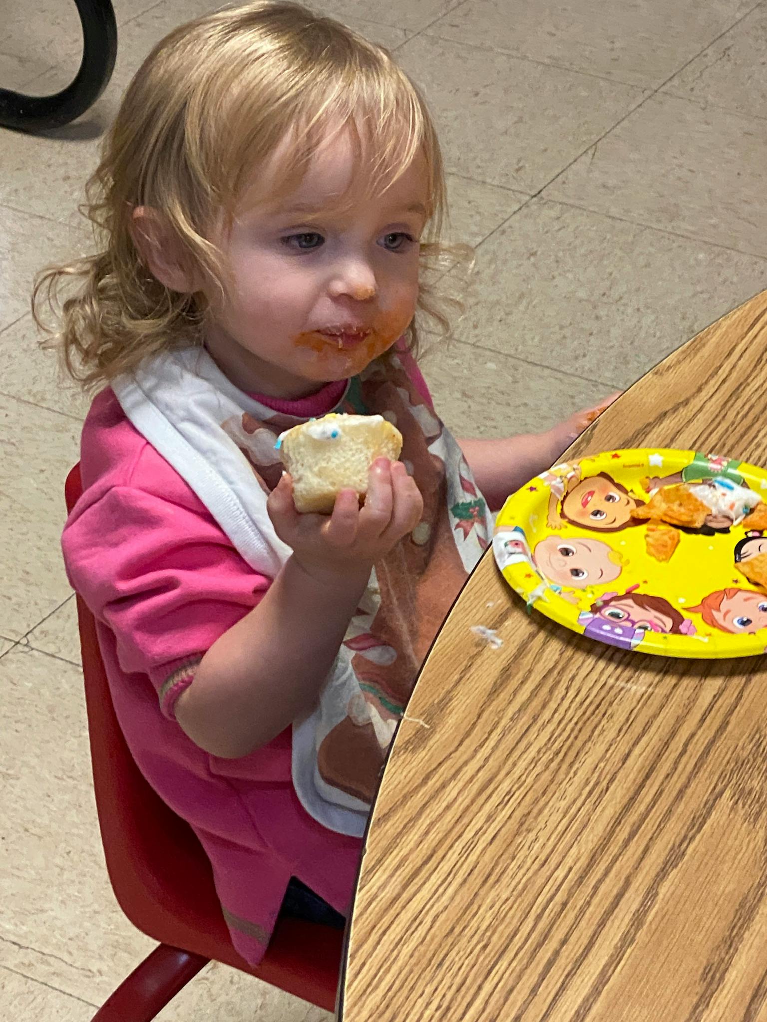 Child with food on face holding a cupcake