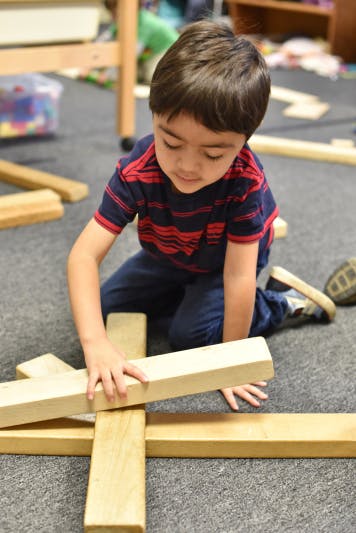 Child kneeling on floor, building with wooden blocks